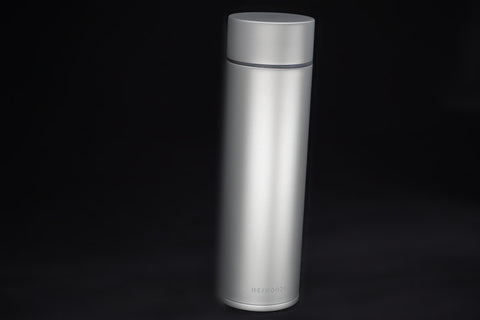 Slim titanium insulated bottle, 450 ml, standing on black with its flat lid on