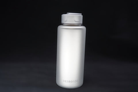 Titanium sport bottle, 700 ml, standing on black, the HEXMONDE wordmark near the base