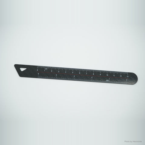 Black carbon fiber ruler with printed centimeter and inch scales, on light gray