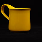 Yellow mug on black, side view with the handle loop to the left and the rim curving slightly outward