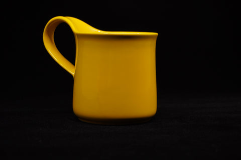 Yellow mug on black, side view with the handle loop to the left and the rim curving slightly outward