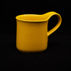 Yellow mug on black, three-quarter view with the handle to the right and the thumb rest rising above the rim