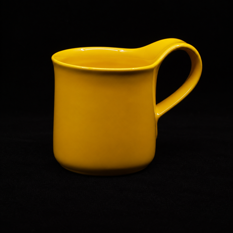 Yellow mug on black, three-quarter view with the handle to the right and the thumb rest rising above the rim